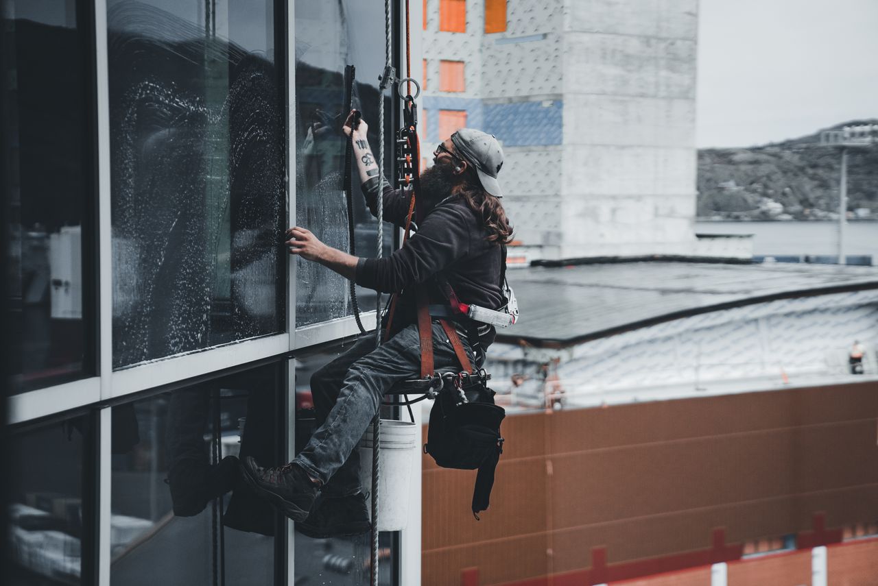 hero-img A man cleaning skyscraper windows with a harness, showcasing urban high-rise work.