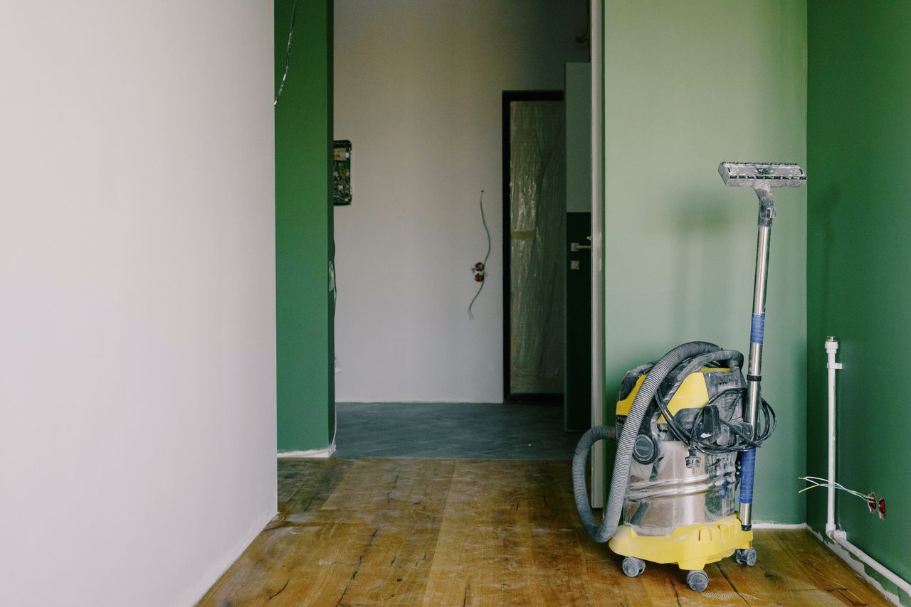 about-01 Industrial vacuum cleaner placed on dirty parquet in room with green walls and doorway in spacious apartment during repair works